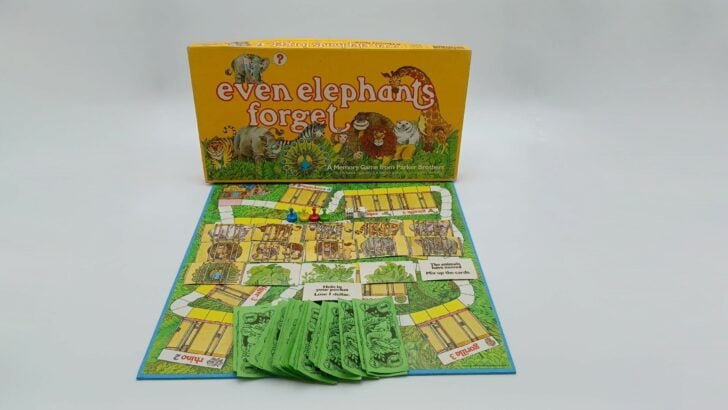 A shot of all of the components included in Even Elephants Forget, including the box, game board, a set of money, 16 cards, four tokens, and two dice.
