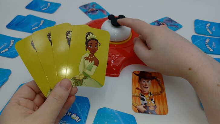 This picture depicts a player with four Tiana cards in their left hand. Their right hand is about to ring the bell.