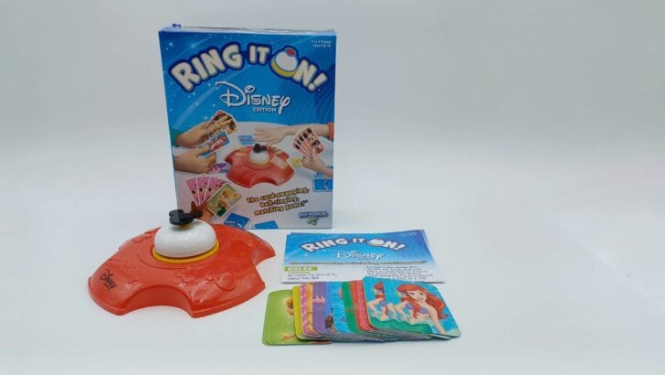This picture shows all of the components of Ring It On!: Disney Edition including the box, the red game tray with bell on top (the bell is mostly white with black Mickey Mouse ears on top), the instructions, and the cards.
