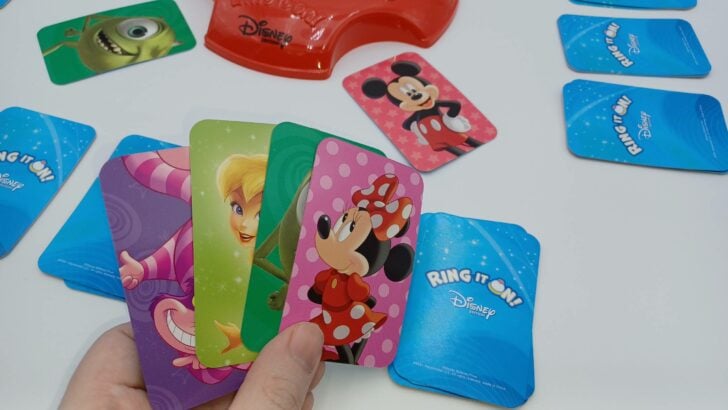 This picture shows the player laying down their pile to look at another one. This hand includes a pink Minnie Mouse card, a green Mike Wazowski card, a light green Tinker Bell card, and a purple Cheshire Cat card.