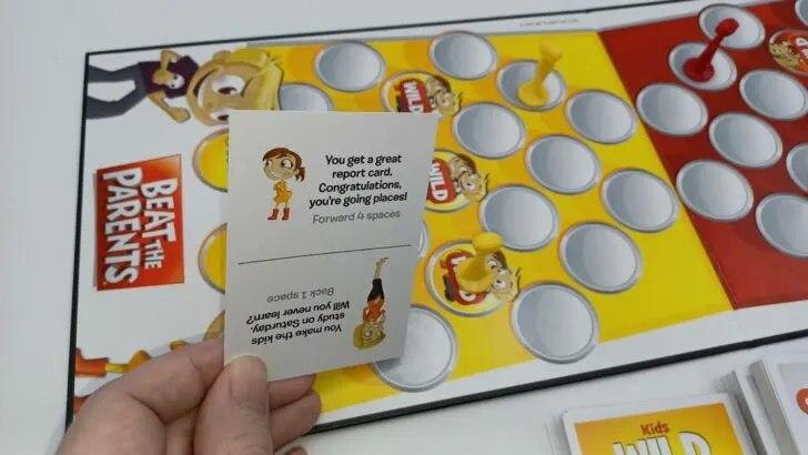 This picture shows the yellow kids team landing on their own Wild Card space. The card they drew says "You get a great report card. Congratulations, you're going places! Forward 4 spaces." They will do what the card says and move their token four more spaces.