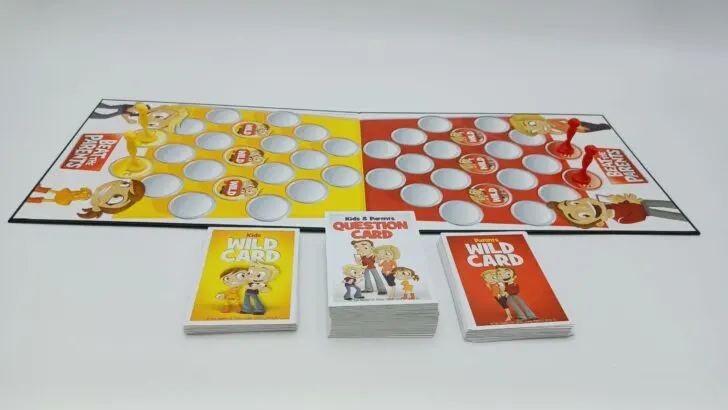 A look at the setup for Beat the Parents featuring the board with two red movers on the two red start spaces and two yellow pawns on the two yellow start spaces. Three decks of cards have also been sorted, shuffled, and laid out by the board.