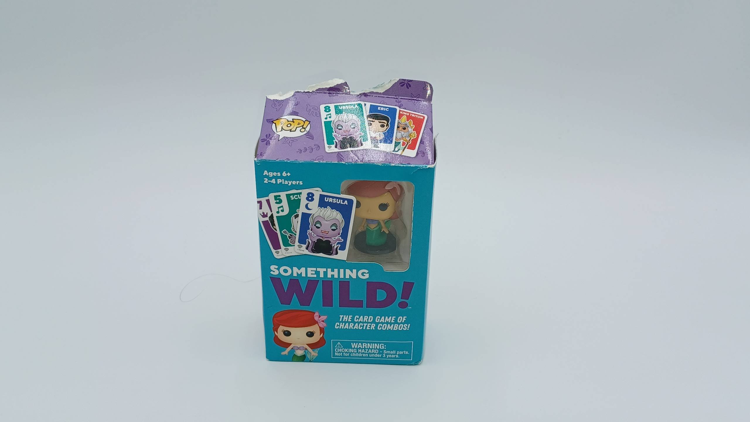 A picture of Something Wild!: The Little Mermaid's box featuring three cards, the text "Something Wild! The Card Game of Character Combos!," a picture of the figure included, and a cut-out portion of the box allowing you to see the figure.