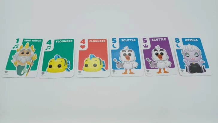 This picture shows a player with six cards in front of them: a green one (King Triton), two Flounder cards (a green and red one), two Scuttle cards (blue and purple), and a blue eight card (Ursula). Since they have more than the five allowed, they will have to discard one card.