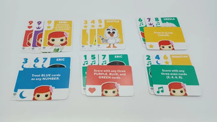 This picture shows six different examples of scoring. The first example shows three Ariel/nine cards (a set). This is followed by a run of three yellow cards, using a Power card to turn a purple seven into the green seven needed for a run, using a Power card to turn a blue three into a blue five to complete a run, a Power card that allows you to score with just any three green cards, and one that allows you to score with any three even cards.