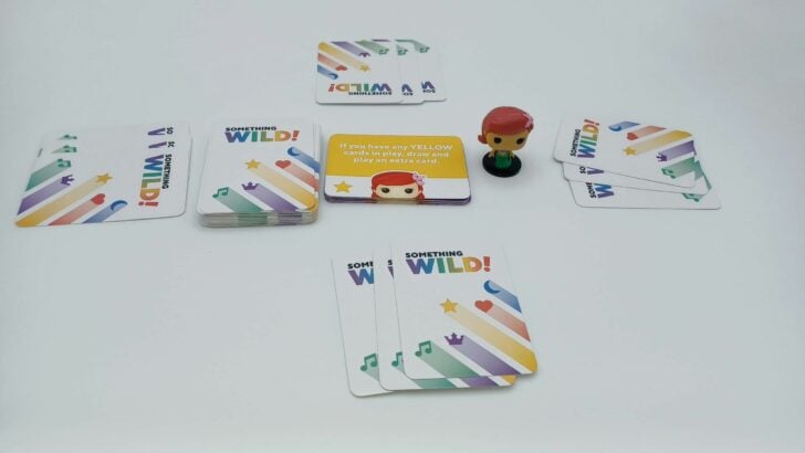 This picture shows how to setup a game of Something Wild!: The Little Mermaid, with a draw deck, a Power card deck (with top card revealed), and the Ariel figure in the middle and four hands dealt out to the players.