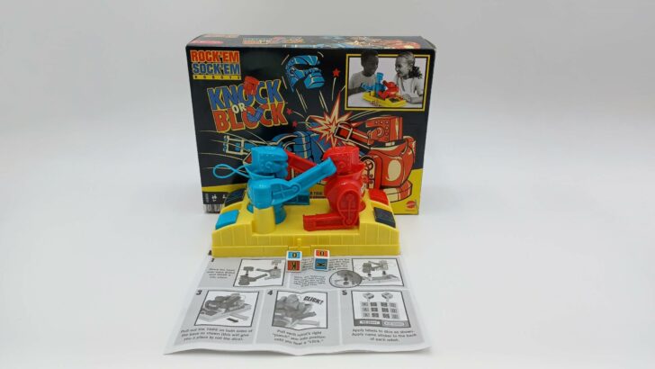 A picture of all of the components included in Rock 'em Sock 'em Robots: Knock or Block. They include a game base, two robots, 2 dice, and instructions.